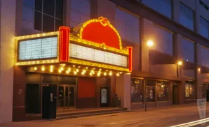 Marquee of a classic movie theater at night, with glowing lights and a red and gold canopy.