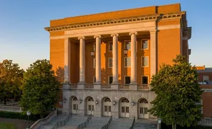 Exterior view of a brick building with large columns and arched doorways at sunset.