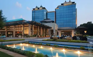 Modern hotel with blue glass towers, a glass-covered entrance, and a water fountain in the foreground.