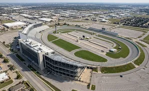 Aerial view of a race track complex with grandstands, parking lots, and surrounding industrial buildings.