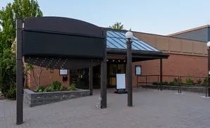 A dark digital sign stands in front of a brick building with a glass-paneled roof.