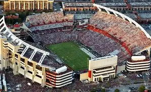 Aerial view of a packed football stadium with red and white seating and a green field.