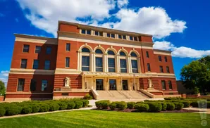 Brick building with arched windows and a manicured lawn under a blue, cloudy sky.