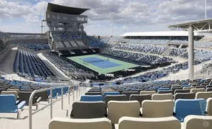 An empty tennis stadium with blue and gray seats surrounding a green court.