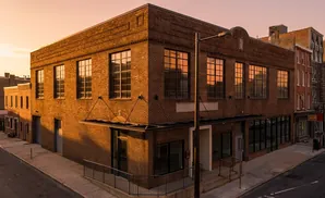 An old brick building with large windows on a city street at sunset.