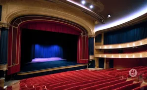 An empty theater with red seats facing a stage draped with red and blue curtains.