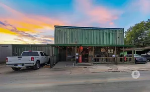 A green building with a covered porch, lit by string lights. A white pickup truck is parked to the left.