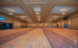 An empty, large ballroom with ornate carpeting, chandeliers, and recessed ceiling panels.