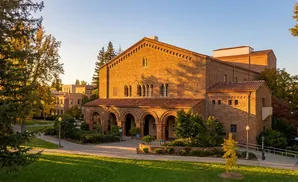 A sunlit brick building with arched doorways and trees on a college campus.