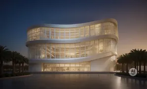 Modern curved building with glass facade and palm trees at dusk.