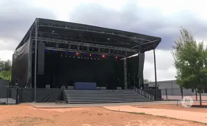 An outdoor concert stage with speakers, lighting, and a large black backdrop.
