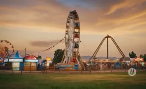 Ferris wheel and amusement park rides at sunset with colorful sky and tents.