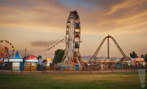 Amusement park at sunset with a Ferris wheel and roller coaster.