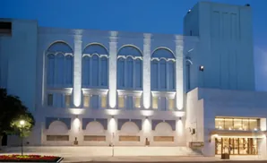 A large, modern white building with arched windows, lit up at dusk.