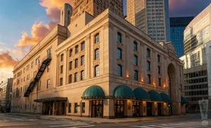 A beige building with green awnings and an American flag on a fire escape, with skyscrapers in the background.