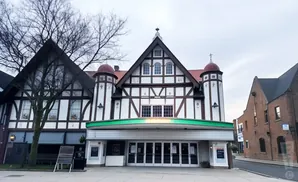 Tudor-style building with a green marquee and glass doors, adjacent to a brick building.