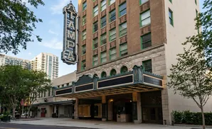 The historic Tampa Theatre marquee, illuminated with lights, stands against a brick building and a light-colored wall.