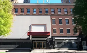 A brown brick building with a large gray section and a red awning.