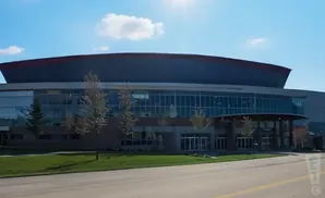 Modern building with a curved roof and large glass windows, set against a blue sky with clouds.