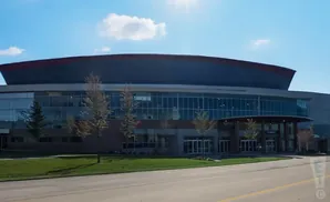 Large modern building with a curved roof and glass facade, surrounded by trees and a lawn.