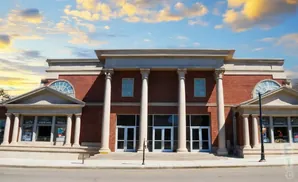 Classical brick building with white columns and arched windows under a cloudy sky.