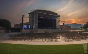Outdoor amphitheater stage with rows of chairs at sunset.