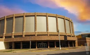 Large circular brick building with tall windows under a colorful sunset sky.