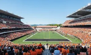 Fans in orange fill a stadium during a sunny football game.