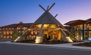 Log cabin-style hotel with a teepee-shaped entrance under a twilight sky.