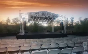 An outdoor stage with seating in front, under a dramatic orange sky.