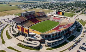 Aerial view of a football stadium with a bright green field, surrounded by parking lots and a suburban neighborhood.