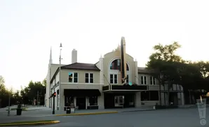 A historic theater with a grand marquee and arched windows, flanked by other buildings and trees.