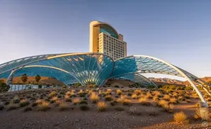 Modern hotel with a large, blue, arched canopy in a desert landscape at sunset.