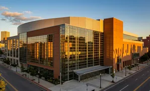 Modern glass and brick building with a curved roof, reflecting the golden sunset and surrounding city skyline.
