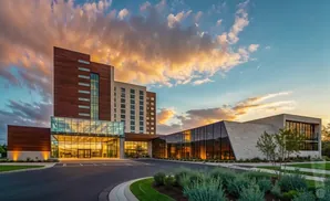 Modern hotel with a glass entrance and contemporary architecture against a dramatic sunset sky.
