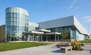 Modern glass and metal building with a curved entrance under a clear blue sky.