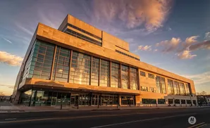 Modern building with stone facade and large glass windows reflecting a sunset sky with clouds.