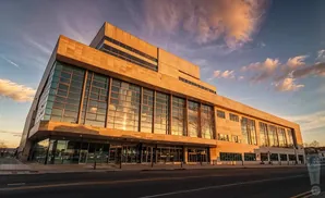 Modern building with large glass windows reflecting a golden sunset sky with clouds.