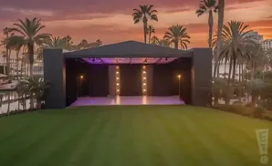 An outdoor stage with palm trees and a sunset sky.