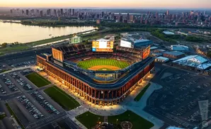 Aerial view of a baseball stadium at dusk, with a cityscape and water in the background.