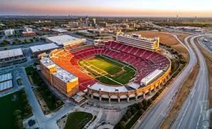 Aerial view of a large, red-seated football stadium at sunset with a cityscape in the background.