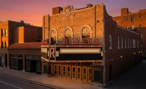The Riviera theater, a historic brick building, is illuminated by a sunset glow, with its marquee lights lit.