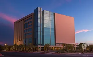 Modern office building with glass facade at dusk, palm trees and pink clouds.