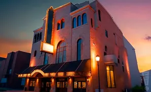 Marquee lights illuminate a historic theater at dusk with a vibrant orange and purple sky.