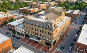 Aerial view of a historic theater building on a tree-lined street in a town square with surrounding brick buildings.