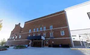 A red brick building with a gabled roof and many windows, with a modern white structure next to it.