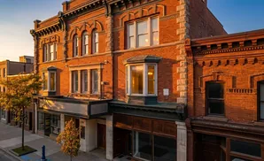 Brick building with bay windows, ornate detailing, and shops on the ground floor, bathed in warm sunlight.