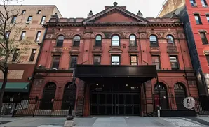 An old red brick building with arched windows and decorative stonework, featuring a dark awning and entrance.