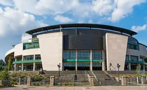 A modern stadium with a curved roof and light-colored stone facade under a blue, cloudy sky.