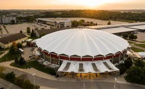 An aerial view of a large domed stadium at sunset, with a parking lot and surrounding buildings.